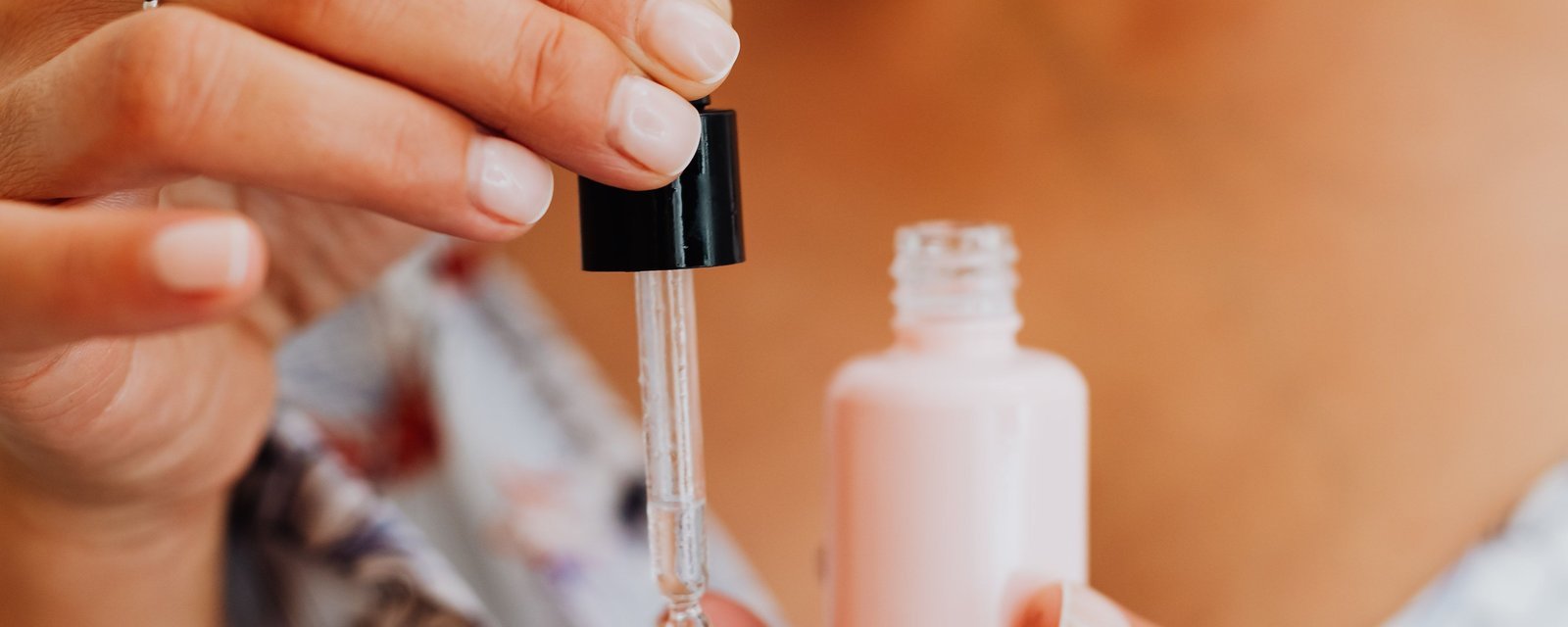 A woman holding a dropper over a small pink serum bottle