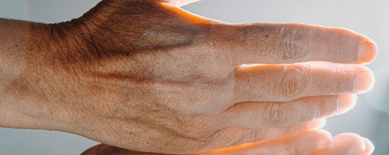 A mature woman's hand held in warm backlight, showing the natural texture and pigment of the skin