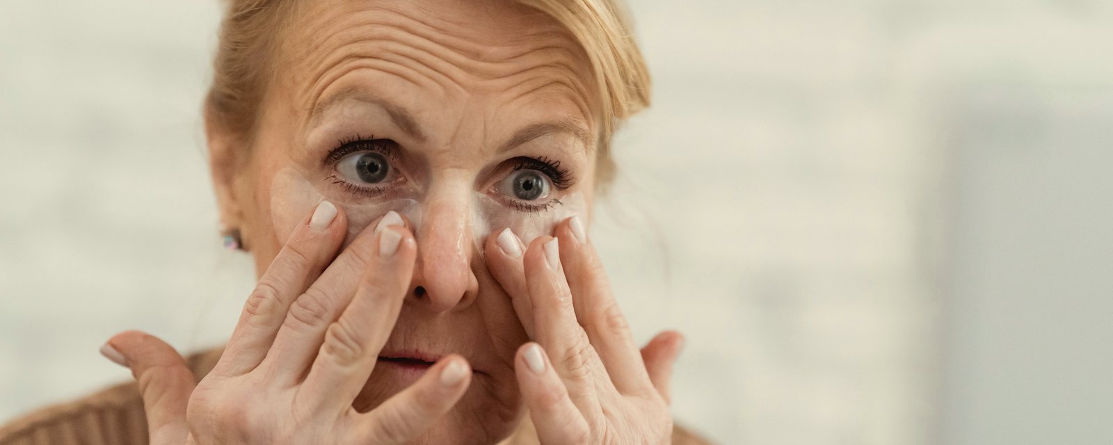 An older woman wiping cream under both eyes with her fingertips