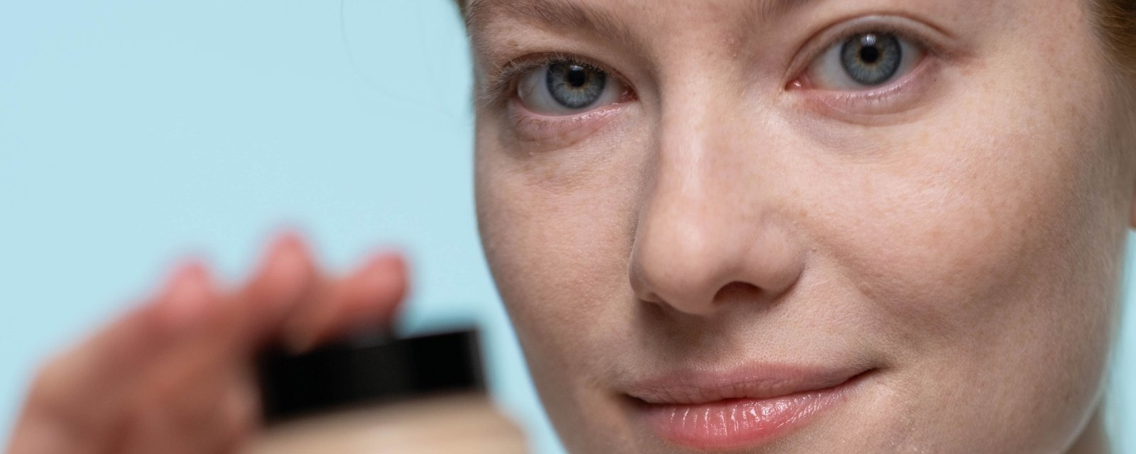 A woman holding a small jar of cream near her face
