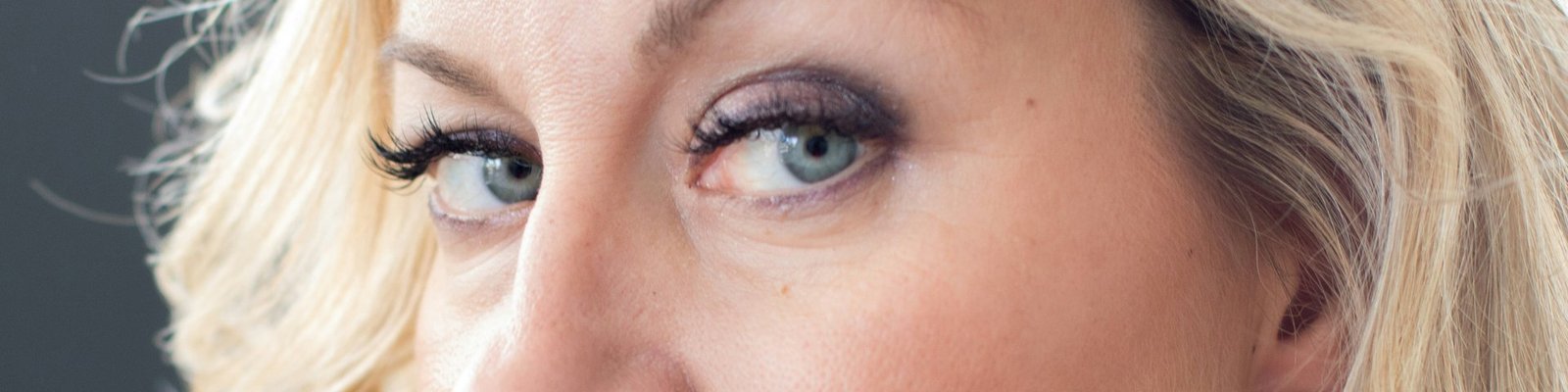 A blonde woman glancing to the side, her blue eyes framed by fine lines