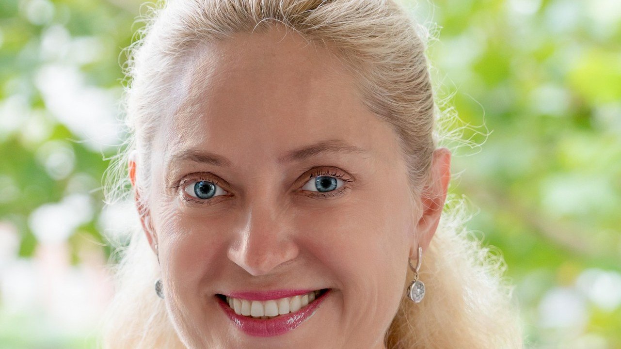 A smiling blonde woman with fine lines at the corners of her blue eyes